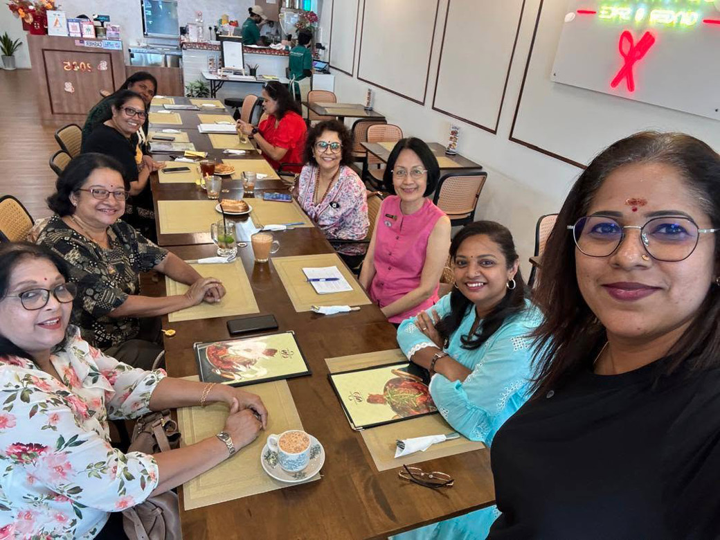 A group of people sitting around a long wooden table in a casual dining setting, smiling and engaging with each other, with menus, cups, and glasses on the table.
Description generated by AI