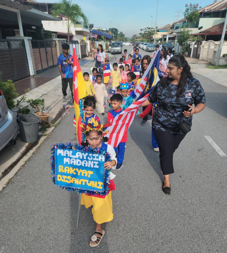 Children and adults are walking down a residential street in a parade, with some children holding flags and a sign that reads "Malaysia Madani Rakyat Disantuni."

Description generated by AI