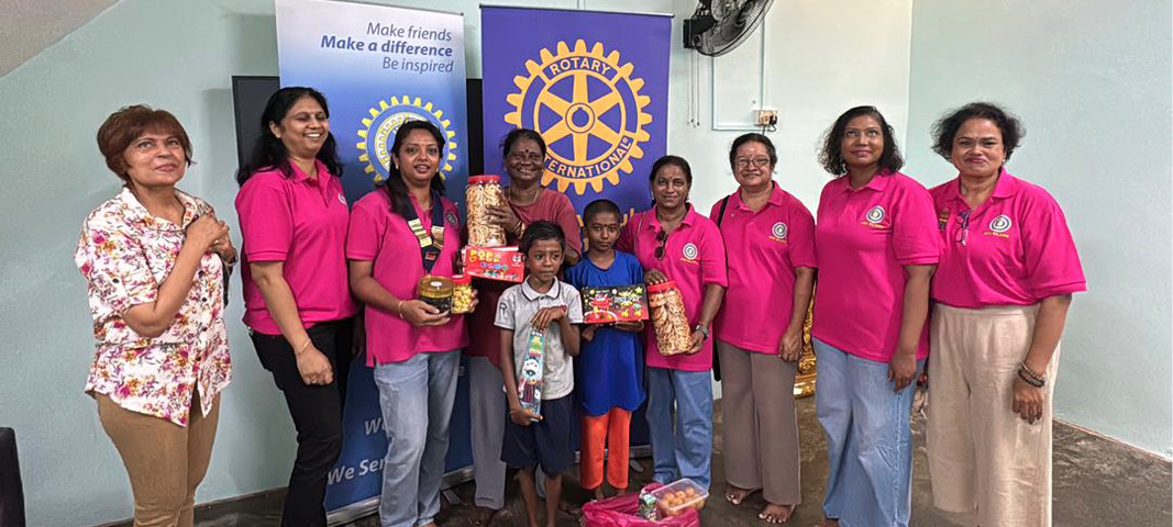 A group of adults and children stand indoors smiling and holding gift boxes in front of two banners with Rotary International logos and motivational text.

Description generated by AI