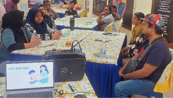 People seated around tables in a classroom or meeting room setting with a laptop and projector displaying a presentation titled "Let's Brain Food."
Description generated by AI