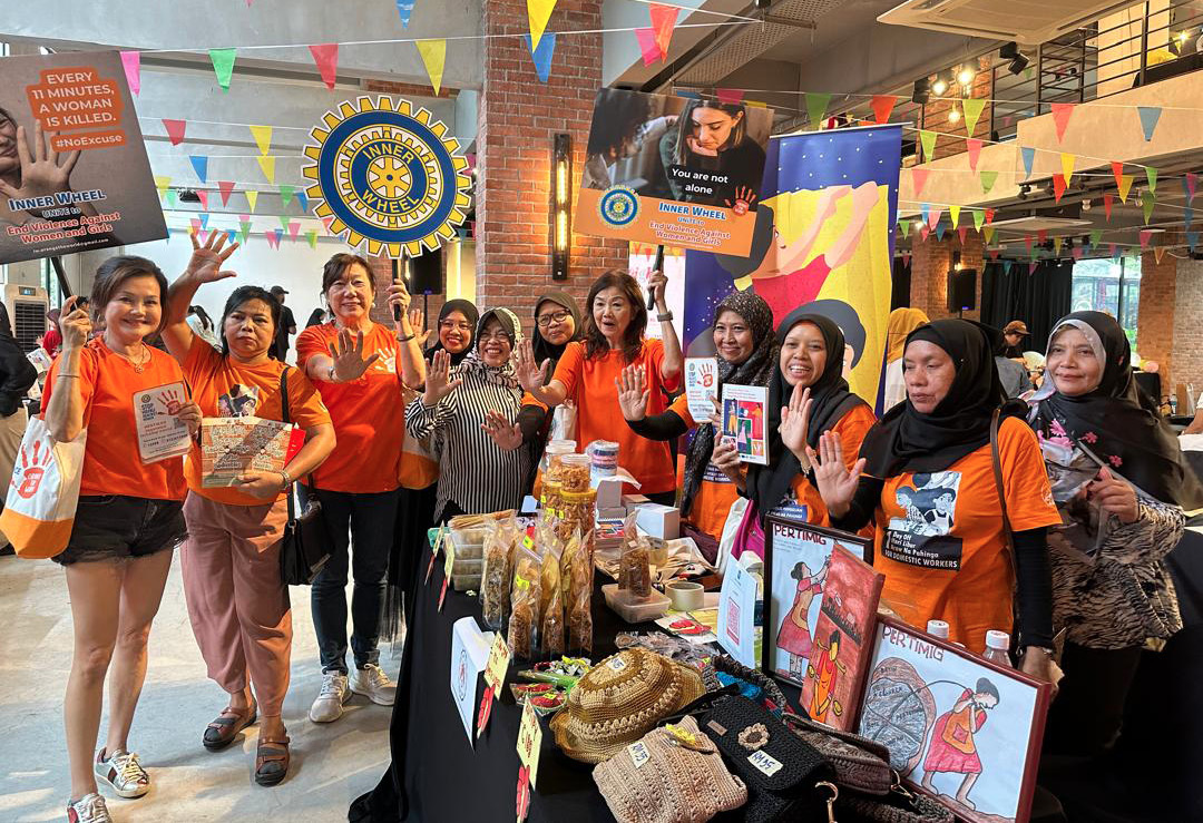 A group of women wearing orange shirts are standing around a table with various items on it.

AI generated content