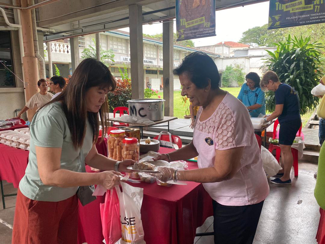Two women are standing at a table with food, one of them is wearing a pink shirt. They are both holding plastic bags.
AI generated content