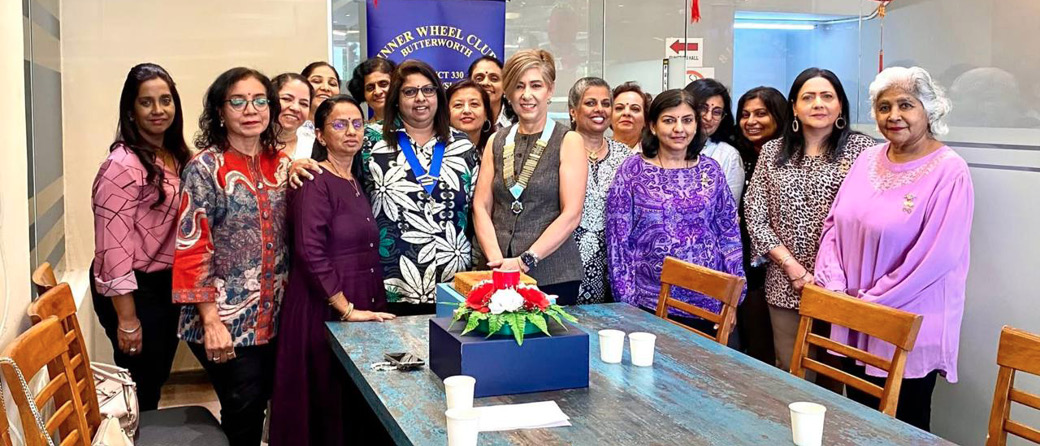 A group of adults standing closely together behind a table with a cake and cups in a brightly lit room decorated with hanging red ornaments.
Description generated by AI