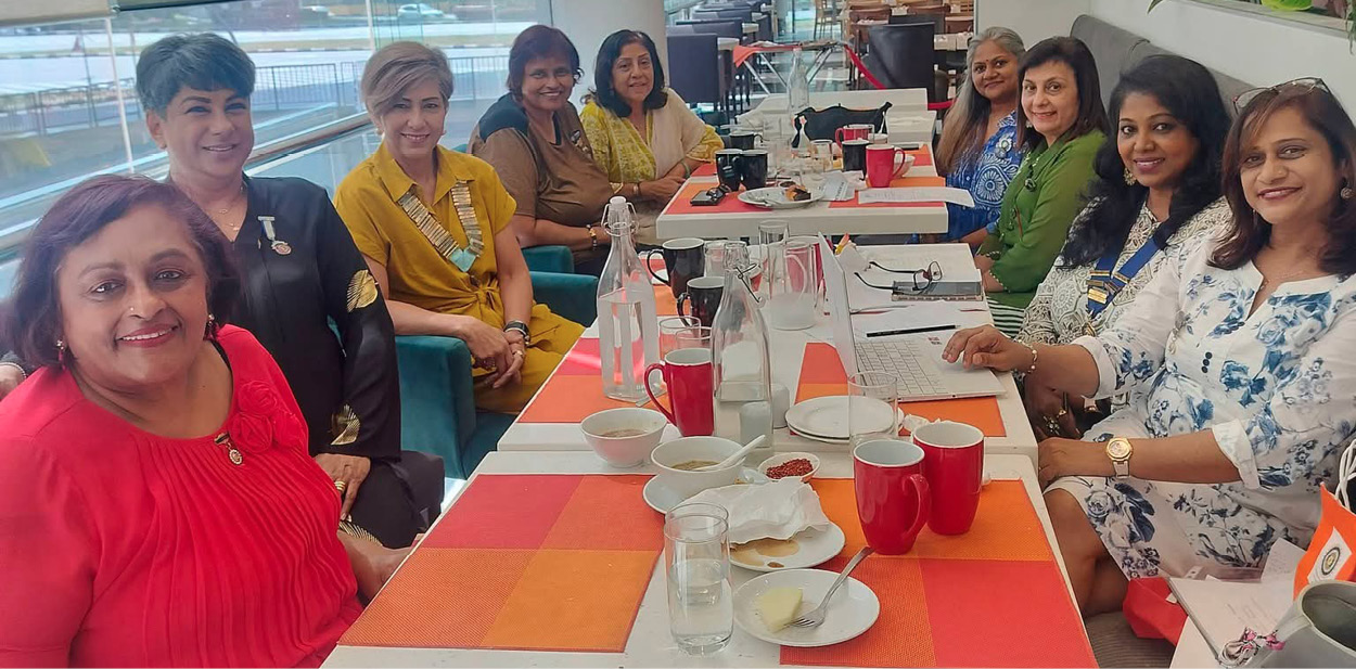 A group of women are sitting around a dining table, posing for a picture. They are wearing colorful outfits and are surrounded by cups, bottles, and a potted plant.
AI generated content