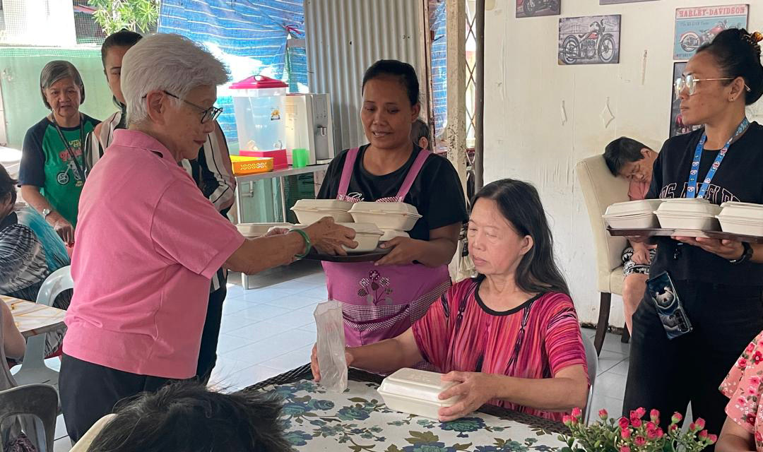 A group of people are gathered around a table with bowls of food. A woman is handing a bowl to a woman sitting at the table. The people are smiling and enjoying the meal.

AI generated content
