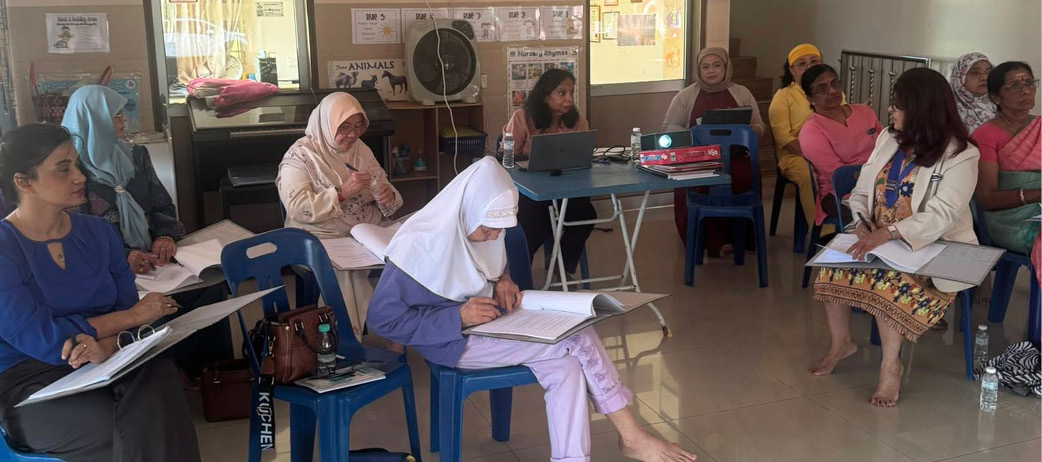 A group of women are sitting on chairs in a room, some of them wearing headscarves. They are engaged in a discussion or activity, with a laptop and a book visible on a table. The women are seated on blue chairs, and there is a handbag placed on the floor. The scene appears to be a casual gathering or meeting.

AI generated content