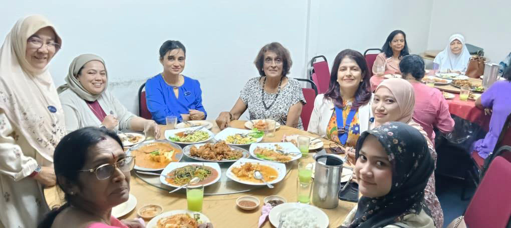 A group of women are sitting around a dining table, enjoying a meal together. They are wearing headscarves and are smiling as they eat. There are several plates of food, including bowls and cups, on the table. The women are seated on chairs, and there are additional chairs around the table. The atmosphere appears to be friendly and social.

AI generated content