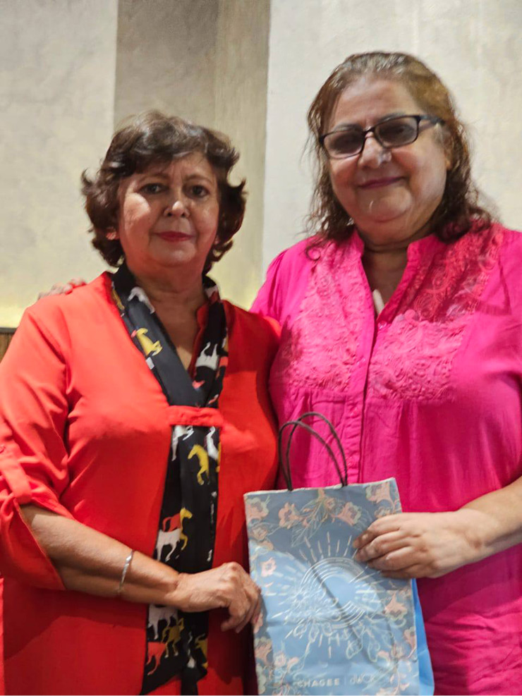 Two adults stand close together indoors with one holding a decorative gift bag while both smile gently.
Description generated by AI