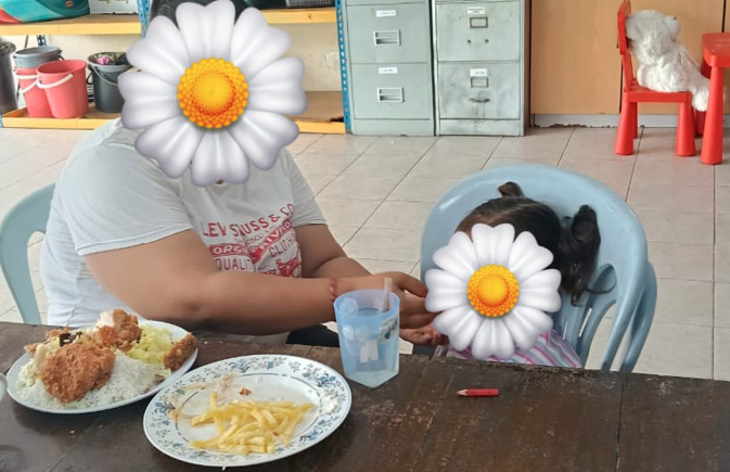 A person sitting at a table with a plate of fried chicken and fries, holding a glass of water, while a small dog sits on a chair next to them.

Description generated by AI