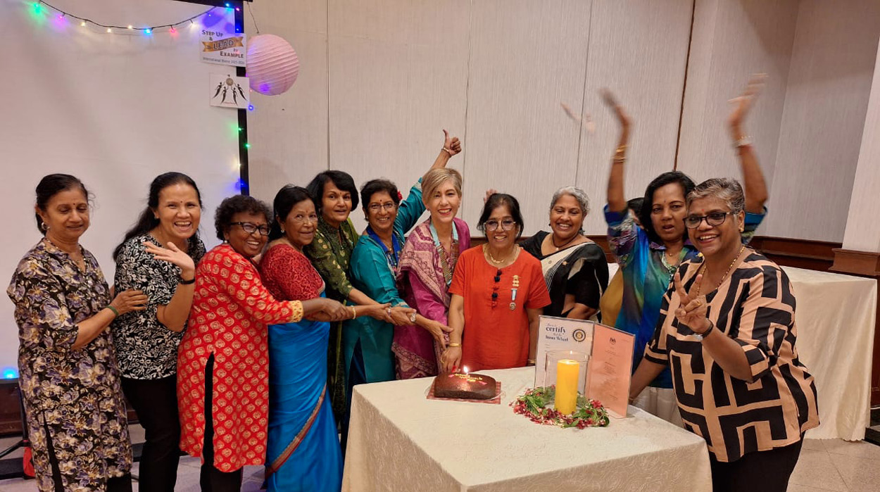 A group of people dressed in colorful traditional clothing are gathered around a table with a cake and a candle, celebrating indoors with some raising their hands in excitement.
Description generated by AI