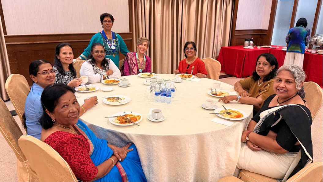 A group of people dressed in colorful traditional clothing are seated around a round table with plates of food and water bottles in a banquet setting.
Description generated by AI