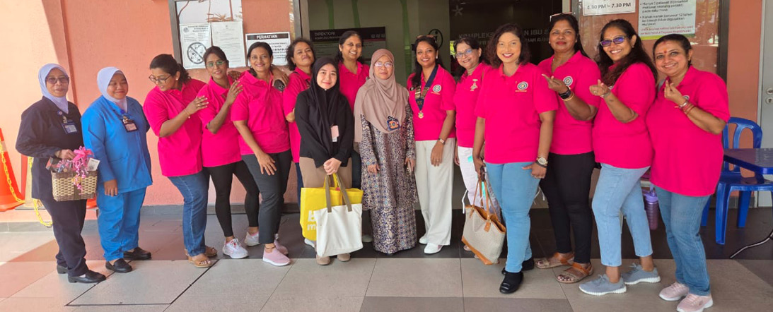 A group of adults wearing bright pink shirts and casual pants stand together smiling in front of a building entrance, with two adults in different attire holding bags in the center.

Description generated by AI