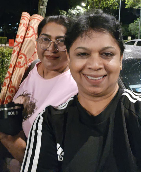 Two adults smiling outdoors at night with one holding rolled-up mats and a tumbler, standing near a tree and parked cars.

Description generated by AI