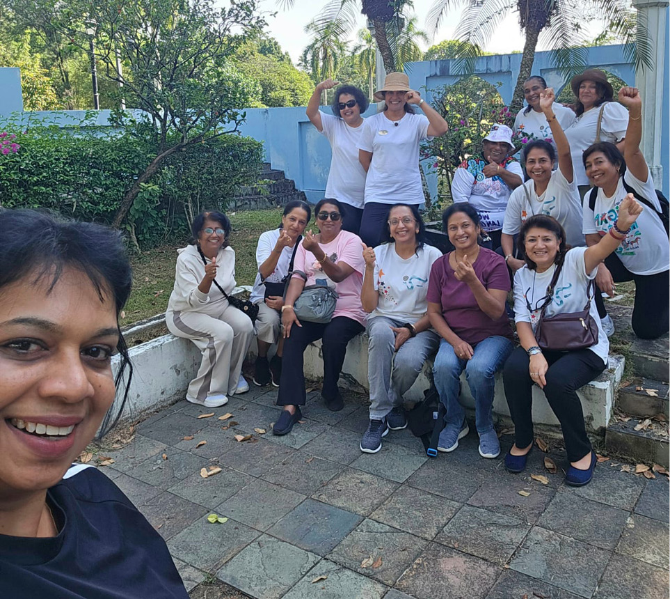 A group of people wearing casual clothes are gathered outdoors on stone steps and pavement, smiling and making cheerful hand gestures while one person takes a selfie.

Description generated by AI