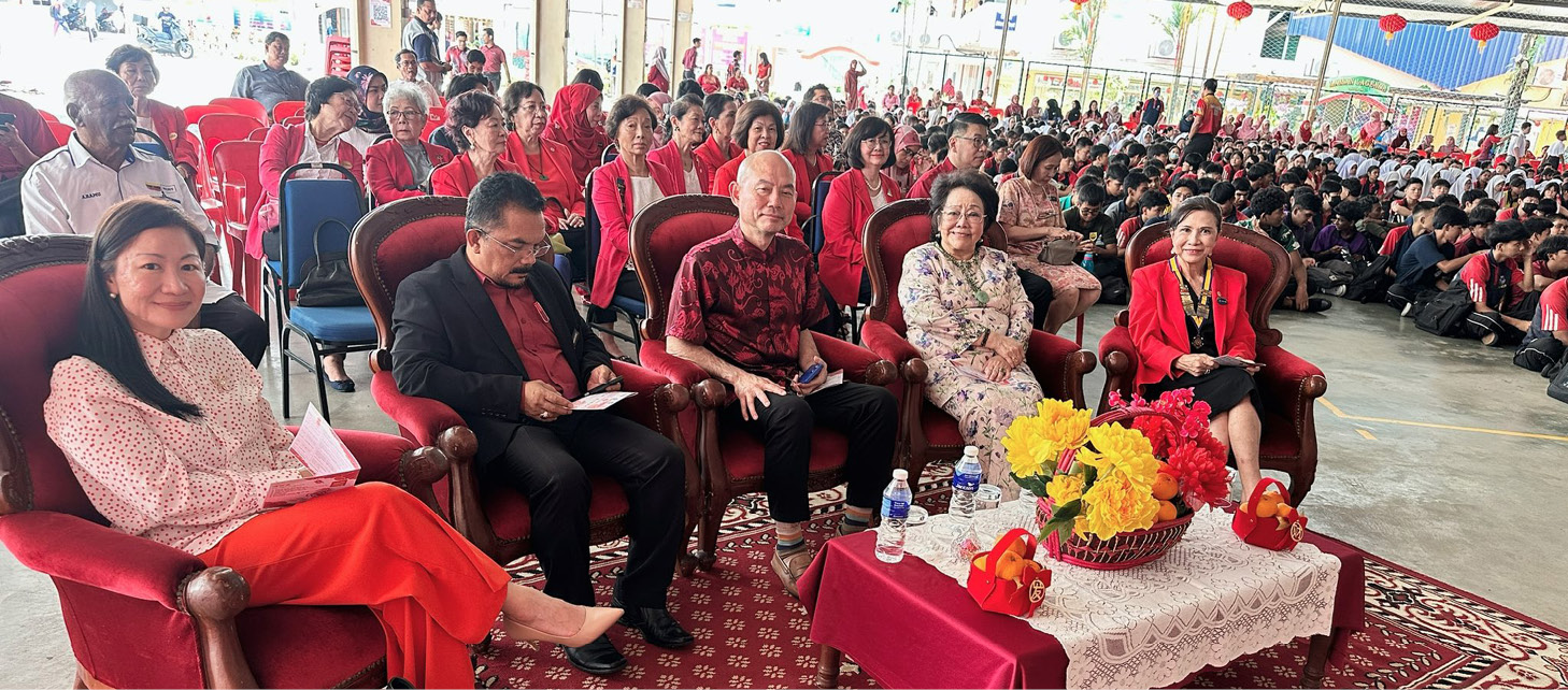 A group of people are sitting on chairs in front of a table with a bowl of flowers. There are four people sitting on chairs, with one person on the left, one in the middle, and two on the right. The people are wearing red shirts, and there are several chairs in the scene. A woman is sitting on the left side of the table, and a man is sitting on the right side. There is a handbag placed on the floor in front of the woman.

AI generated content
