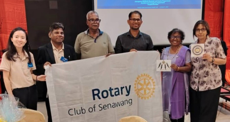 A group of six people stand indoors holding a Rotary Club of Senawang banner in front of a presentation screen displaying information about stroke awareness.
Description generated by AI