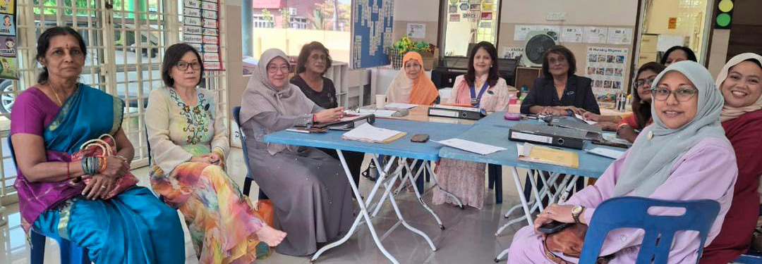 A group of adults wearing colorful traditional and modern clothing are seated around a table in a bright room decorated with educational posters and banners.
Description generated by AI
