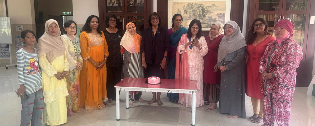 A group of people dressed in colorful traditional and casual clothing stand indoors around a small table with a cake on it, smiling for a photo.
Description generated by AI