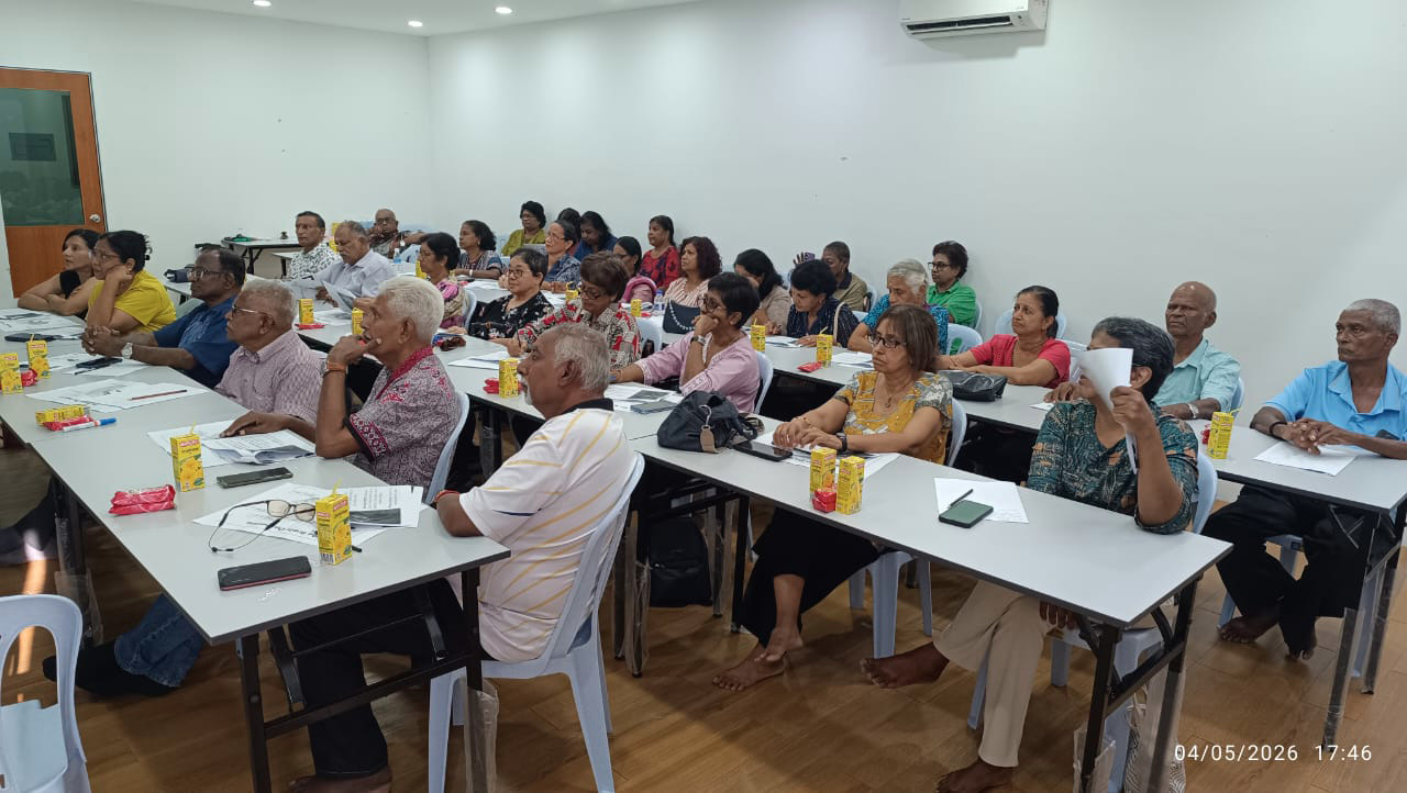 A group of adults and seniors are seated in a classroom setting, attentively listening and taking notes with papers and drinks on the tables.
Description generated by AI