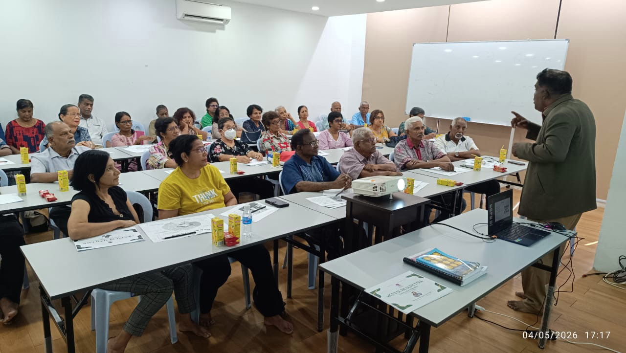 A group of adults seated in a classroom setting attentively listening to a person standing and speaking near a whiteboard.
Description generated by AI