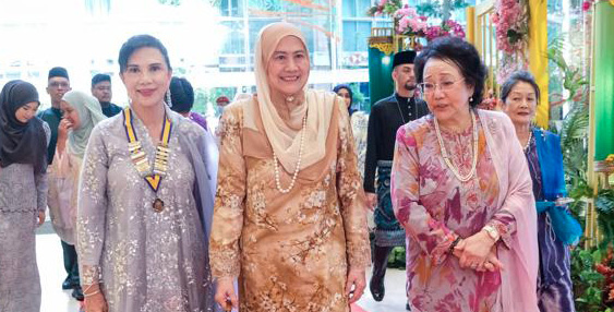 Several adults dressed in traditional attire walk together on a red carpet inside a decorated indoor venue near an entrance.
Description generated by AI