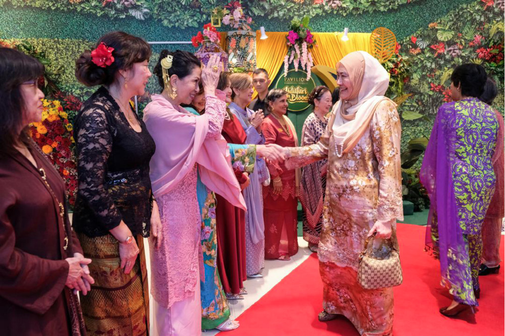 People dressed in colorful traditional clothing are greeting each other warmly on a red carpet in a decorated indoor setting.
Description generated by AI