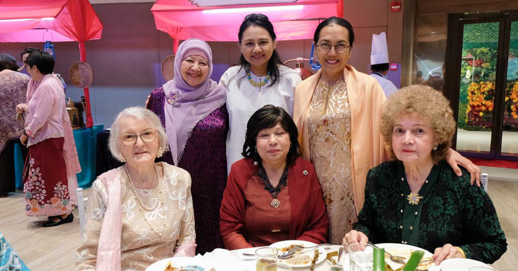 Six adults dressed in a mix of traditional and modern clothing are gathered around a table with plates of food in a banquet setting with a pink stall labeled Maharaja in the background.
Description generated by AI