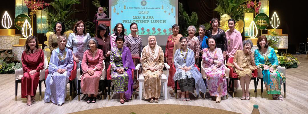 A group of adults dressed in colorful traditional attire are seated and standing on a stage with plants and decorative lights, posing for a formal group photo in front of a screen displaying event information.
Description generated by AI