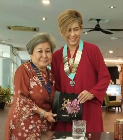 Two adults wearing traditional clothing and medals stand together smiling while another person in purple takes a photo of them in a restaurant setting.
Description generated by AI