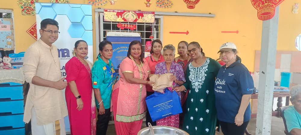 A group of adults standing indoors in colorful traditional and casual clothing are smiling and holding gift bags and a wrapped package.
Description generated by AI