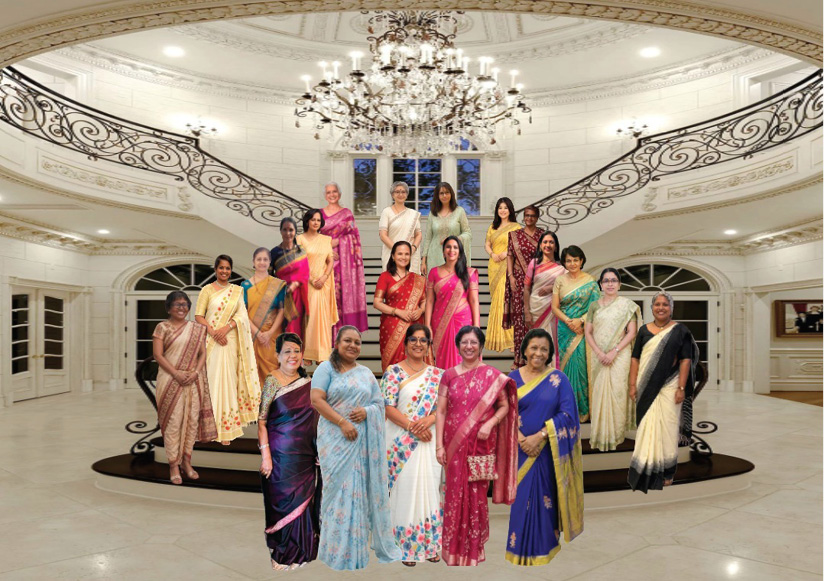 A group of adults dressed in colorful traditional sarees are standing together on a staircase inside an elegant, well-lit room with ornate railings and a large chandelier.
Description generated by AI