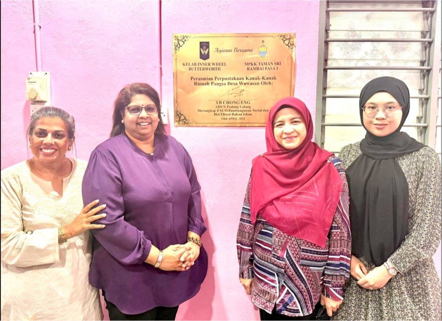 Four adults stand smiling in front of a pink wall with a yellow plaque, wearing colorful and patterned clothing including a headscarf and glasses.

Description generated by AI