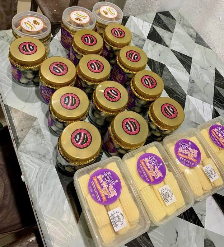Several jars with gold lids and purple labels are arranged on a reflective surface next to plastic containers holding baby corn.
Description generated by AI