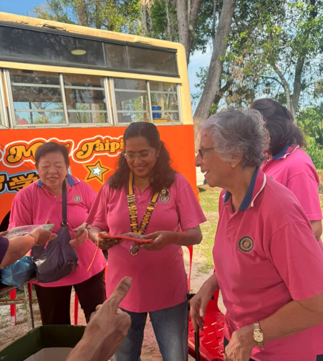 Several adults wearing matching pink shirts are gathered outdoors near a colorful bus, engaging in a friendly interaction involving handing out items.
Description generated by AI