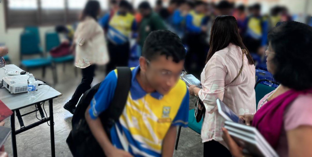 People wearing colorful uniforms and casual clothing are gathered and interacting in a room with chairs and tables.
Description generated by AI