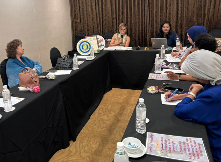 People seated around a U-shaped table engaged in a meeting with papers, water bottles, and a laptop on the table.
Description generated by AI