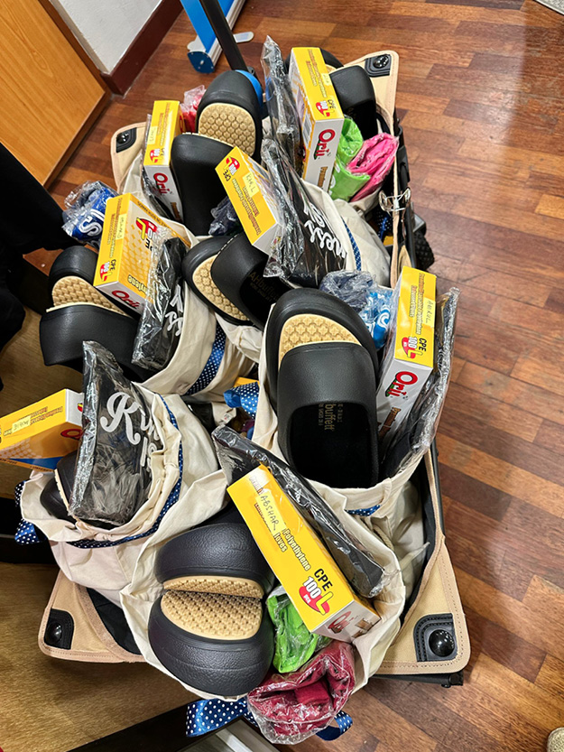 Several pairs of black and beige sandals are neatly arranged in beige fabric bags, each accompanied by a yellow box of shoe insoles, all placed on a wooden floor.
Description generated by AI