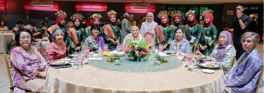 A group of people dressed in traditional attire are gathered around a large round table with a floral centerpiece in a banquet hall.
Description generated by AI