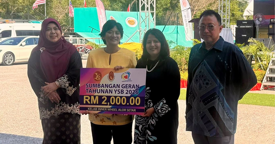Four adults stand outdoors holding a large sign displaying a monetary amount, with a stage and musical instruments visible in the background.
Description generated by AI