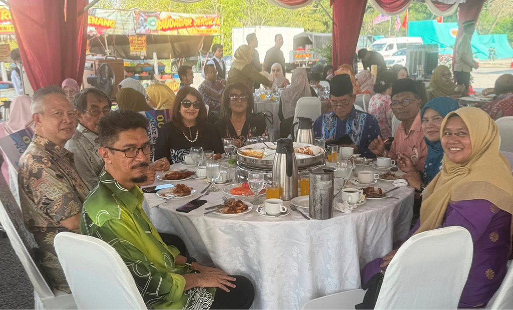 A group of people dressed in colorful traditional and casual clothing are seated around a round table covered with a white tablecloth under a decorated tent, enjoying a meal together.
Description generated by AI
