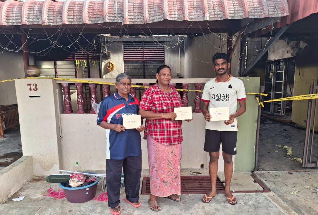 Three adults stand outside a house holding certificates, with one wearing a red plaid shirt and floral skirt, another in a blue and red shirt with dark pants, and the third in a white sports jersey and black shorts.

Description generated by AI