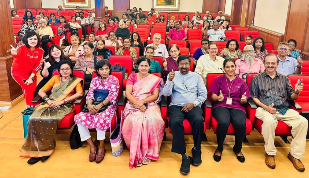 A group of adults seated in red chairs in a conference room are smiling and giving thumbs up while facing the camera.
Description generated by AI