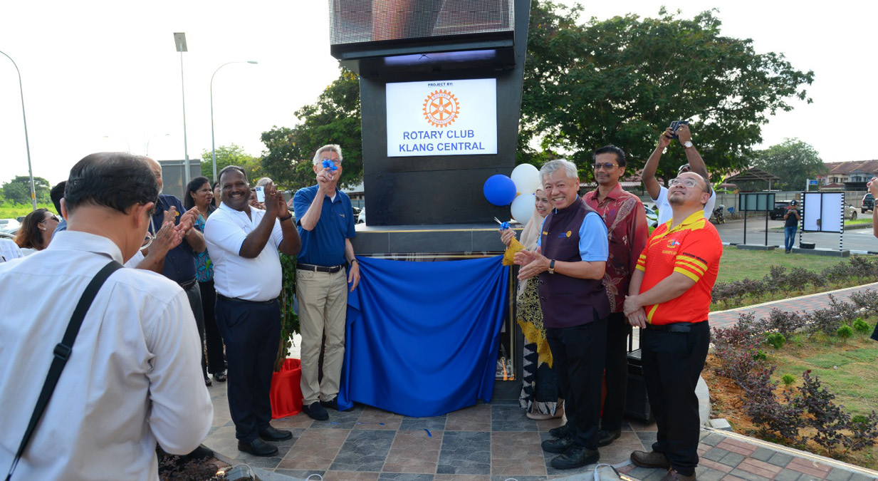 A group of people stands outdoors around a covered plaque with a Rotary Club sign, clapping and smiling during an unveiling ceremony.

Description generated by AI