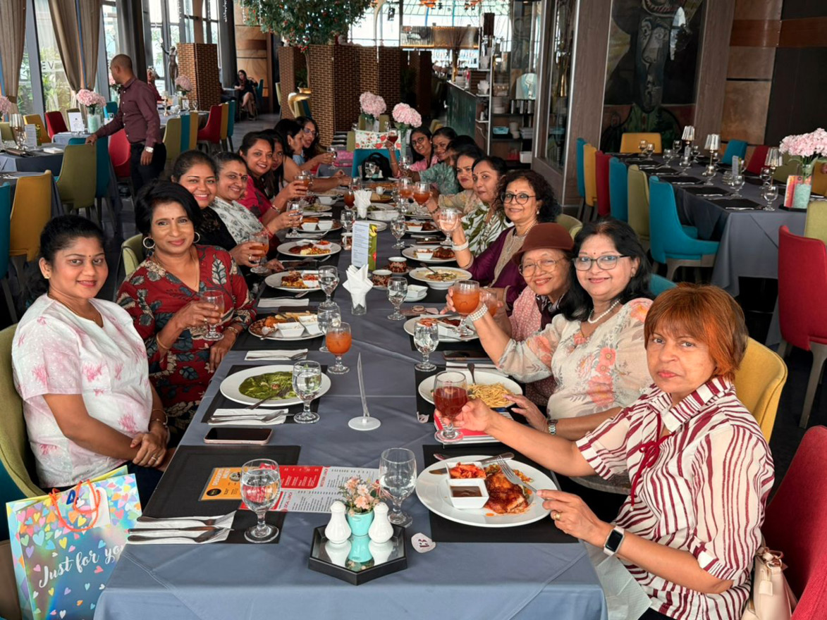 A group of adults seated around a long dining table in a restaurant are enjoying a meal together, raising glasses in a toast with plates of food and drinks in front of them.

Description generated by AI