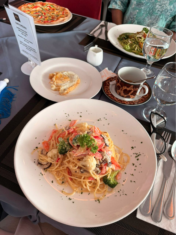 A table set with plates of pasta, a slice of pizza, a cup of coffee, glasses of water, and cutlery arranged on a gray tablecloth.

Description generated by AI