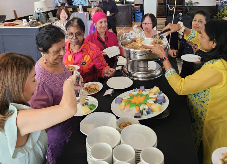 A group of people dressed in colorful clothing are gathered around a table serving themselves food from a buffet in a decorated indoor setting.
Description generated by AI