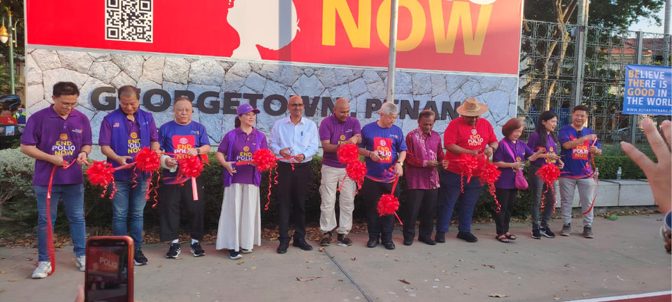 A group of people standing in a line outdoors are holding red ribbons and scissors, appearing to participate in a ribbon-cutting ceremony in front of a large banner.
Description generated by AI