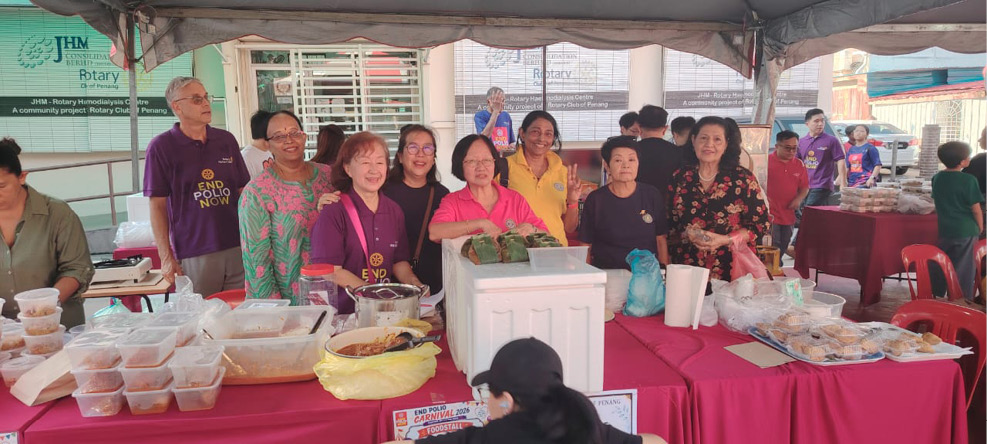 A group of adults standing behind a table covered with a red cloth displaying various packaged food items under a tent at an outdoor market or event.
Description generated by AI