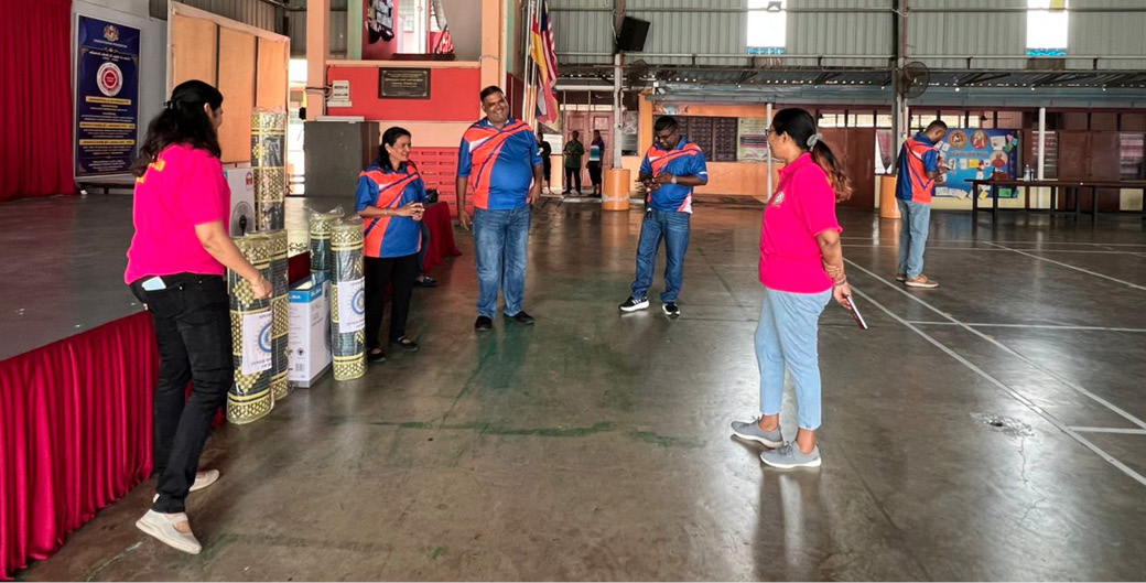People wearing bright pink and blue shirts are standing and interacting in a large indoor space with high ceilings and banners on the walls.
Description generated by AI