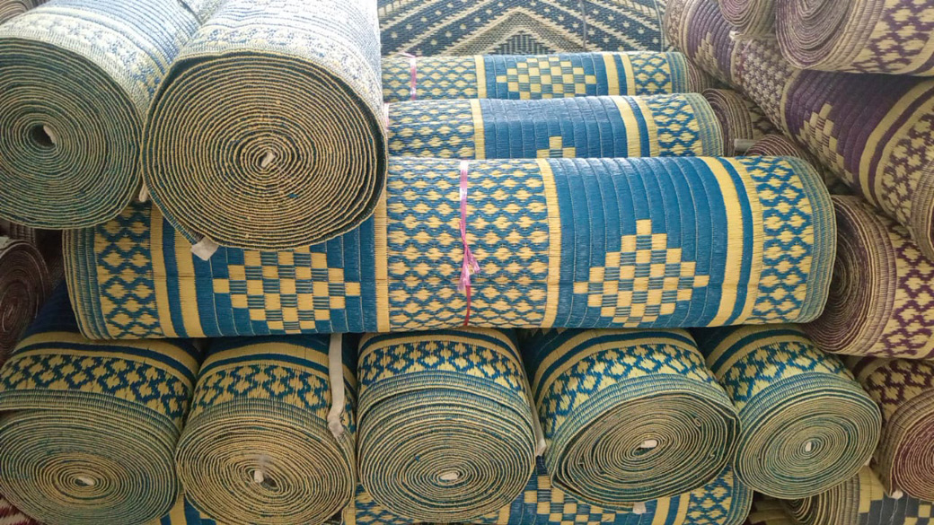 Rolled woven mats with blue, yellow, and purple geometric patterns are stacked closely together.
Description generated by AI